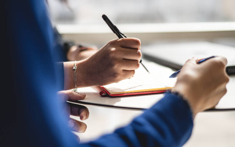 Zoom sur des mains en train de prendre des notes sur des feuilles