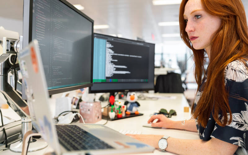 Femme devant 3 écrans d'ordinateur, sur des logiciels de développement