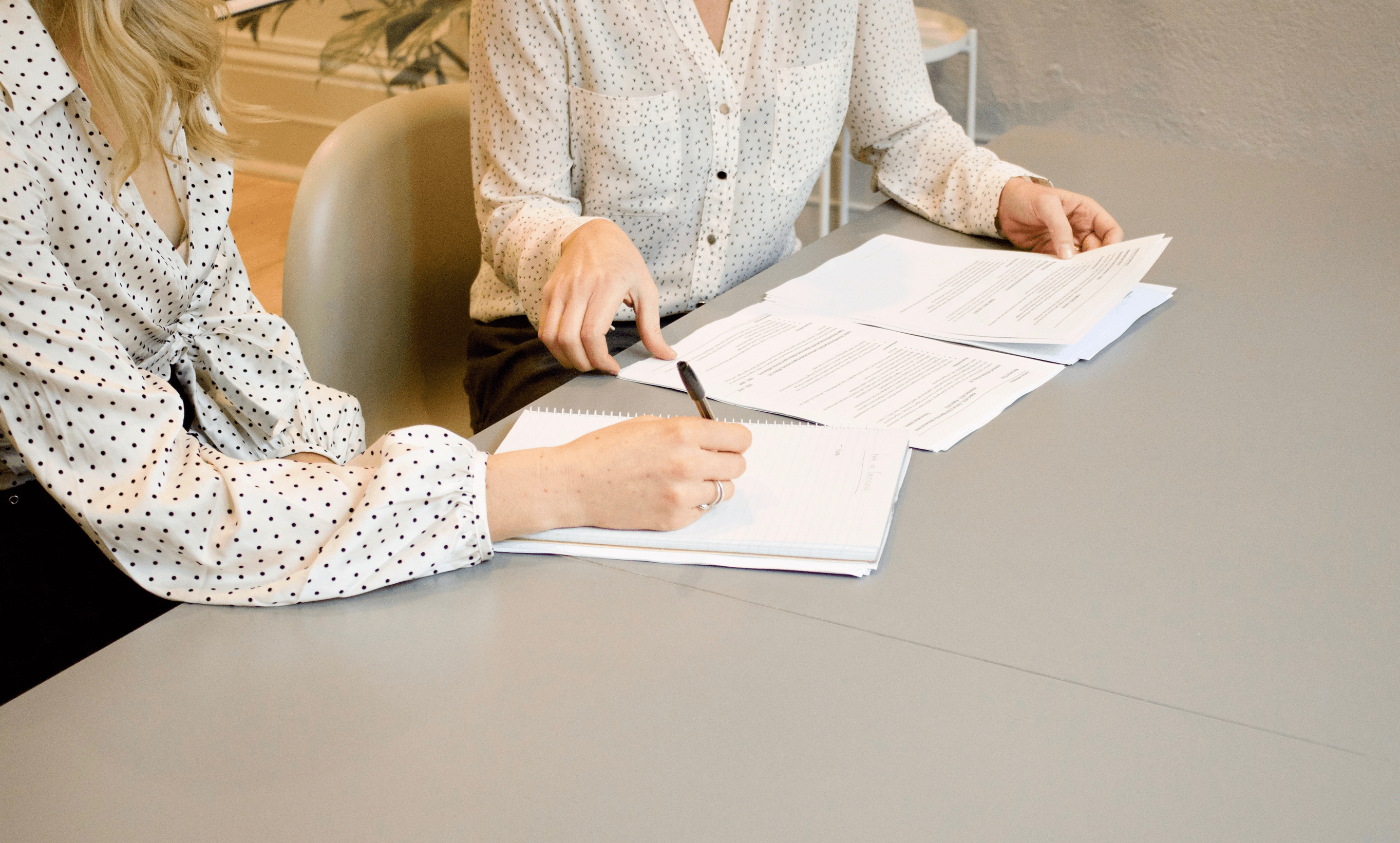 femme signant sur du papier d'imprimante blanc à côté d'une femme s'apprêtant à signer des documents