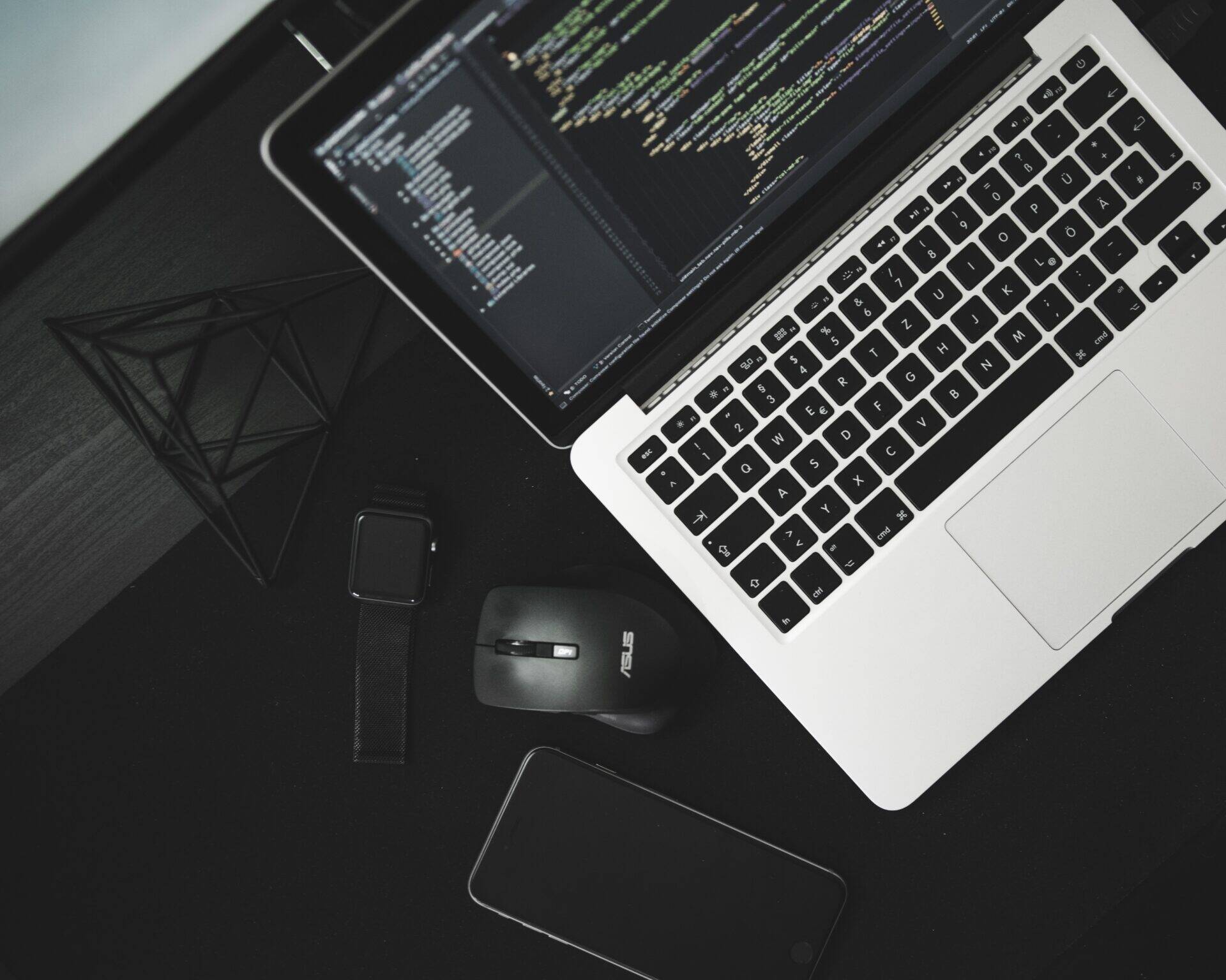 Un ordinateur avec des lignes de code, une souris, un smartphone et une montre connectée en vue plongée