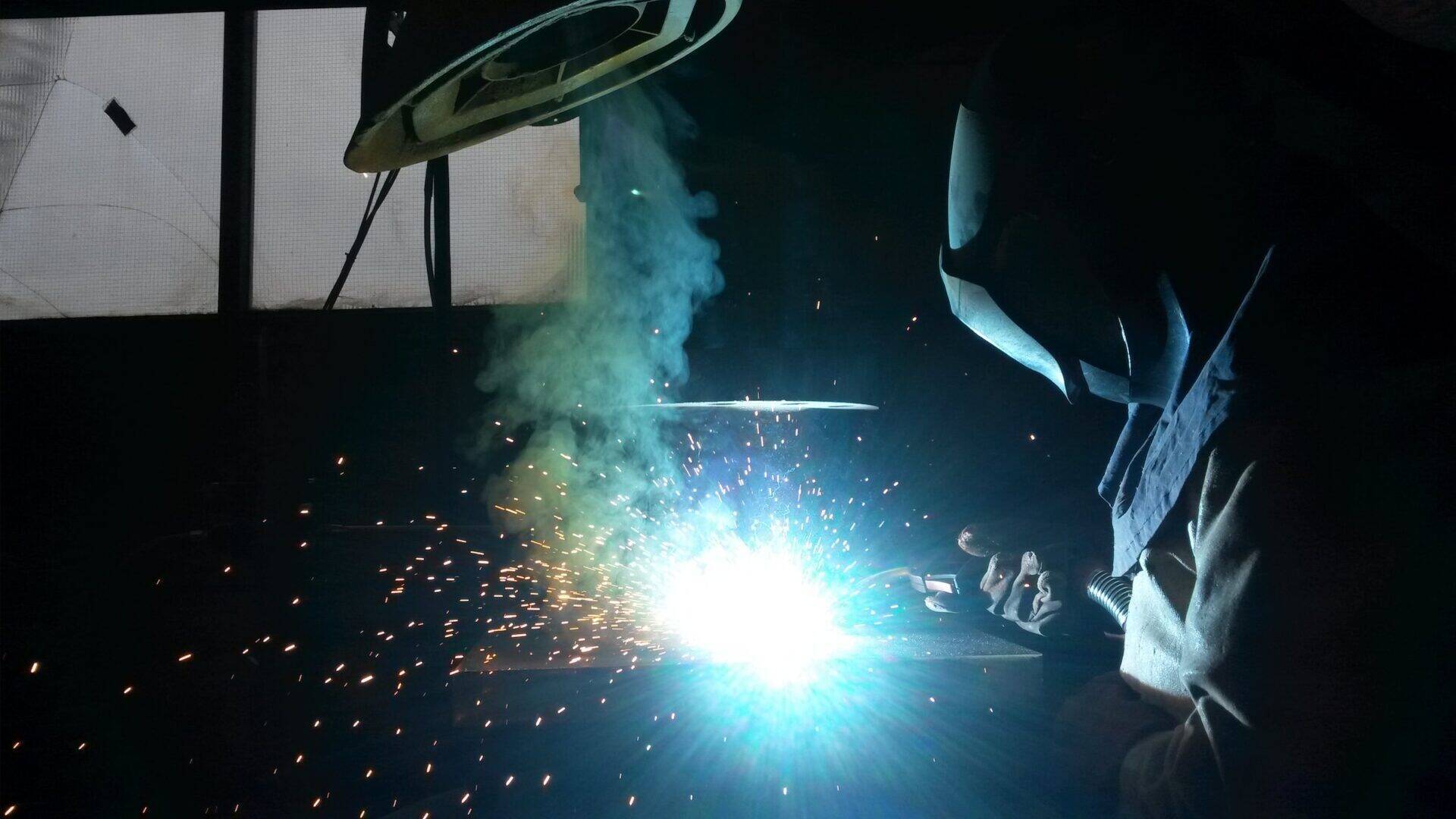 Un chaudronnier en plein travail éclairé par les éclats de sa soudure