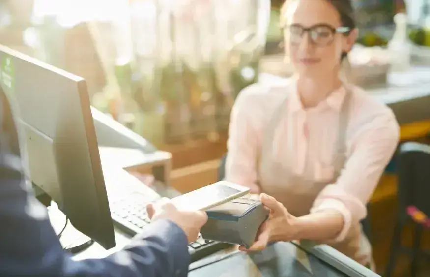 Une gemme tenant un terminal de paiement avec un bras posant son téléphone pour un achat sans contact